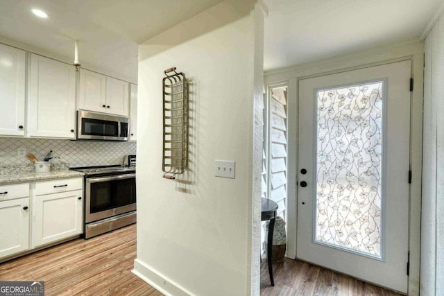 kitchen featuring appliances with stainless steel finishes, backsplash, white cabinetry, and light hardwood / wood-style flooring