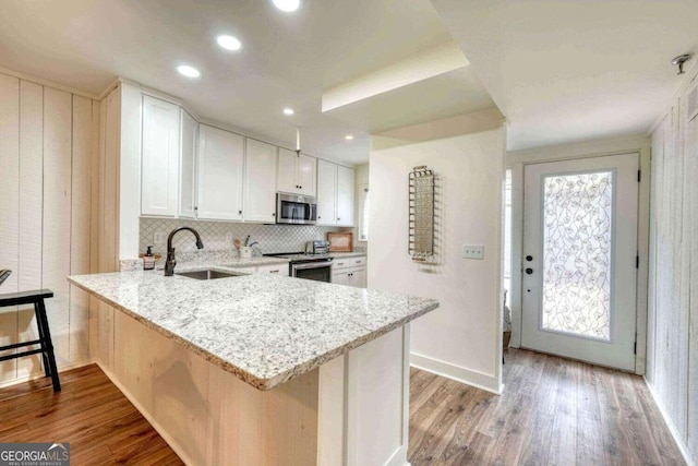 kitchen with appliances with stainless steel finishes, white cabinets, kitchen peninsula, light hardwood / wood-style flooring, and sink