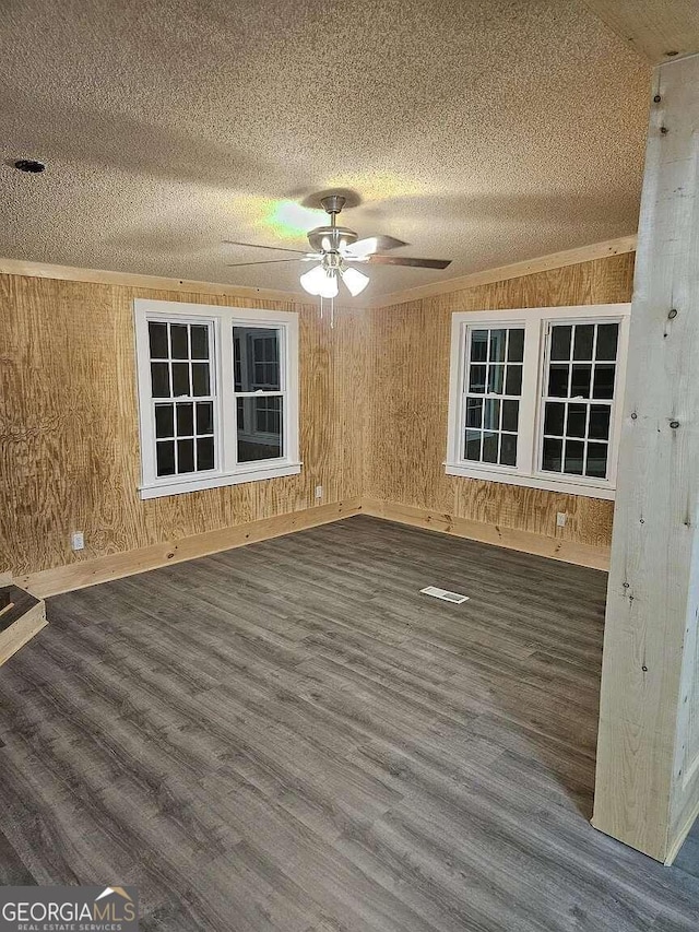 empty room with a textured ceiling, wooden walls, dark wood-type flooring, and ceiling fan