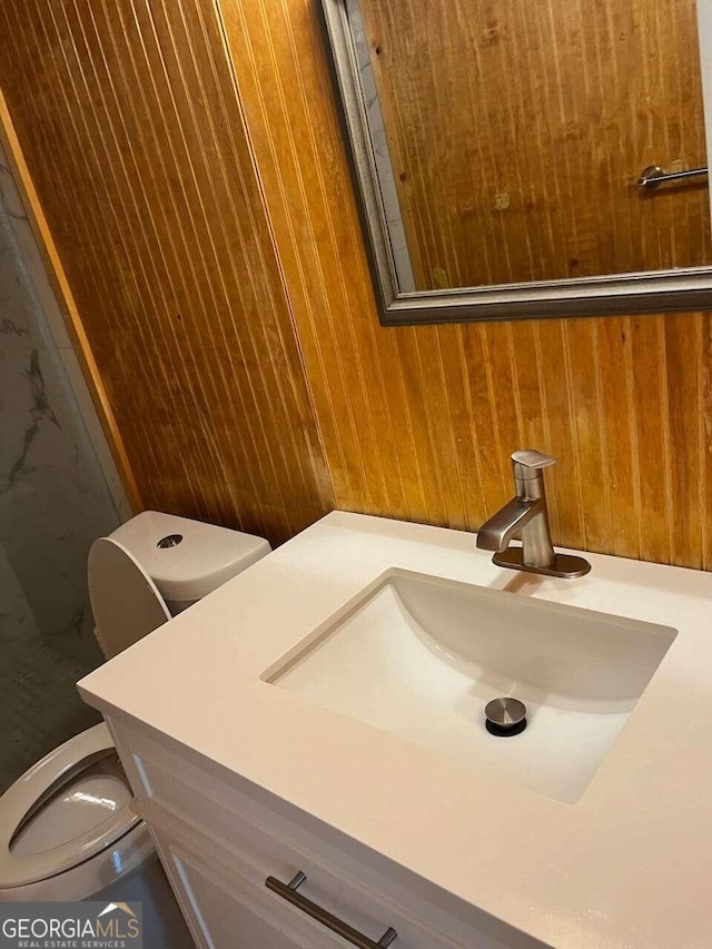 bathroom featuring wood walls, vanity, and toilet