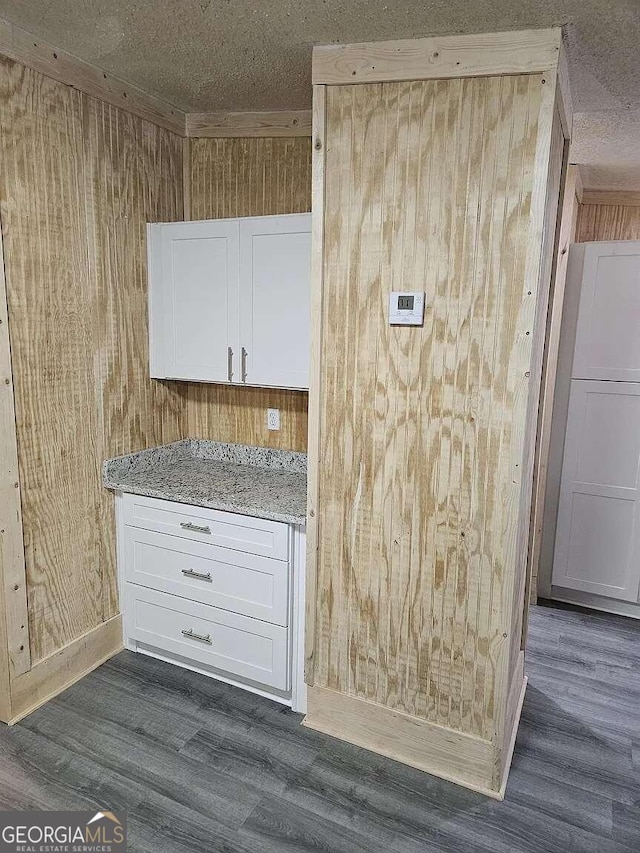 kitchen with wood walls, white cabinetry, dark wood-type flooring, and light stone counters