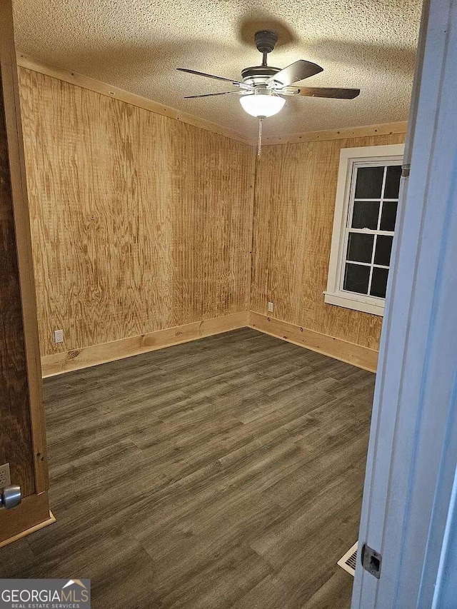 unfurnished room featuring ceiling fan, a textured ceiling, wooden walls, and dark hardwood / wood-style floors