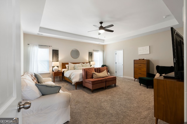 carpeted bedroom featuring a tray ceiling, ceiling fan, and multiple windows