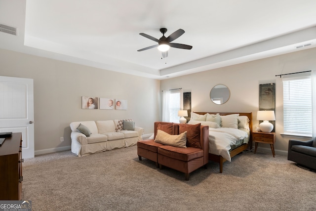 bedroom with ceiling fan, a tray ceiling, and light carpet