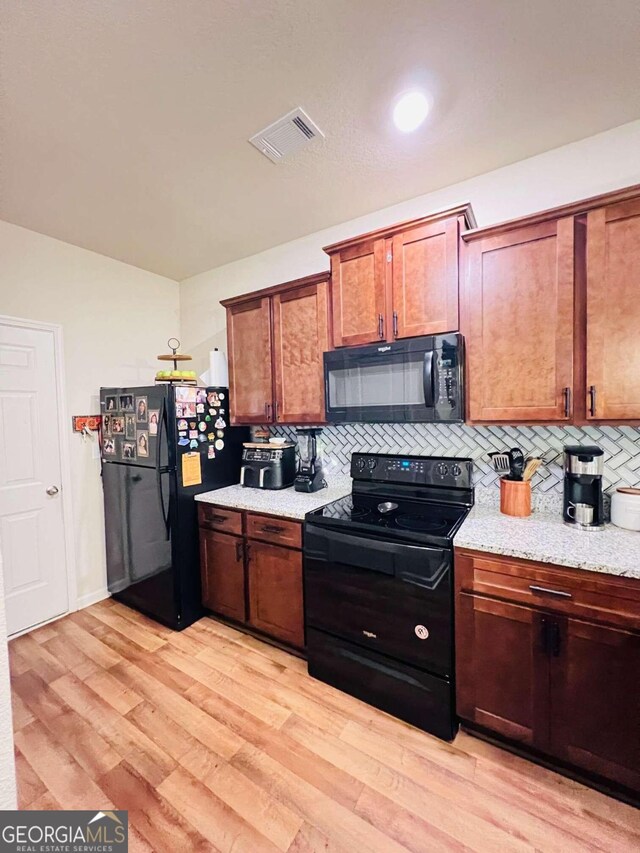 kitchen featuring black appliances, light stone countertops, light hardwood / wood-style flooring, and tasteful backsplash