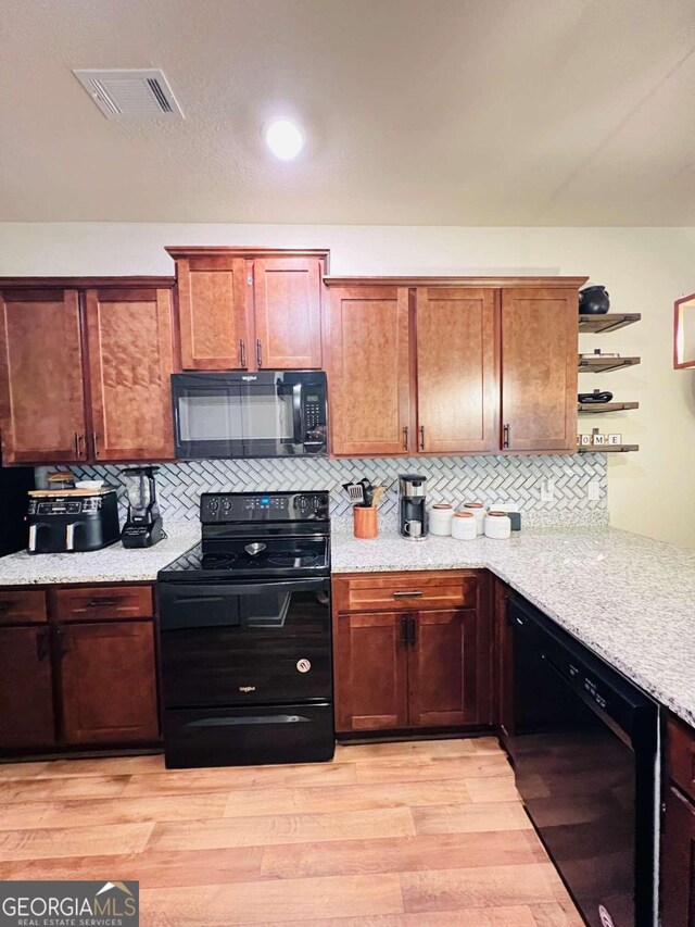 kitchen with light stone countertops, light hardwood / wood-style floors, tasteful backsplash, and black appliances