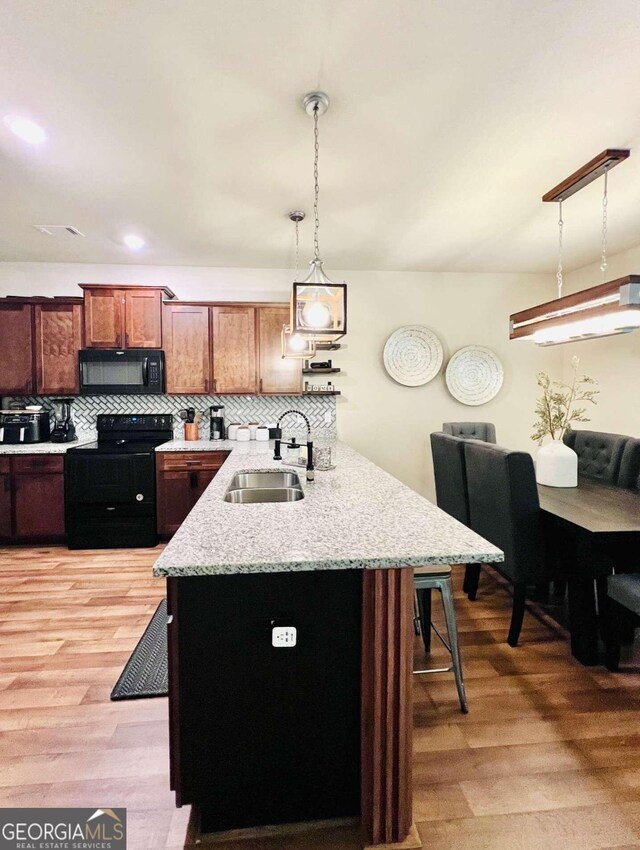 kitchen featuring hanging light fixtures, sink, light hardwood / wood-style flooring, backsplash, and black appliances