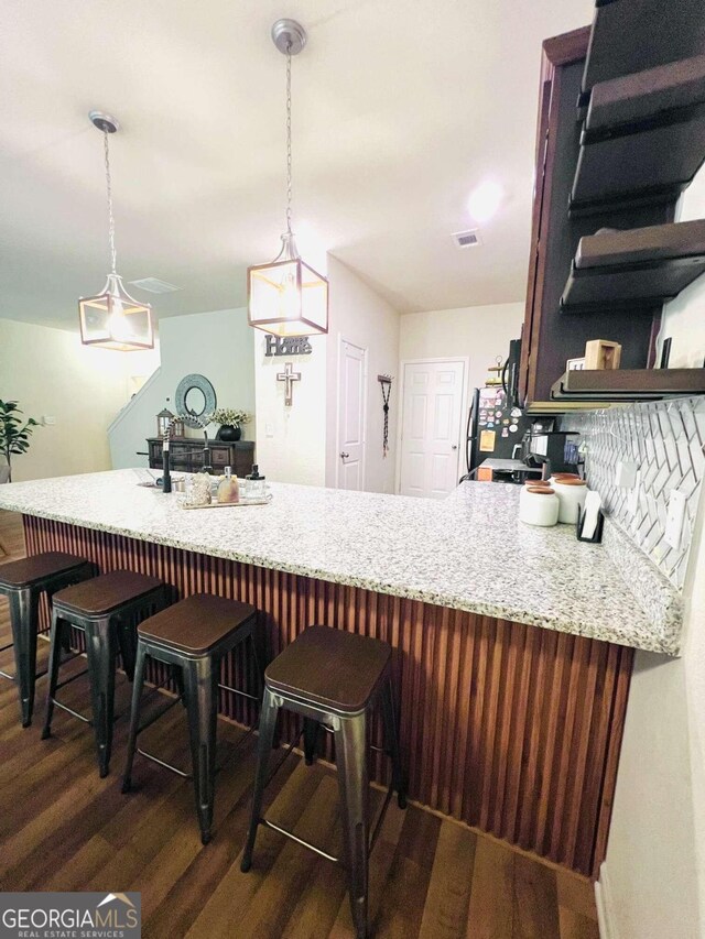 kitchen featuring a breakfast bar area, decorative light fixtures, dark hardwood / wood-style floors, and kitchen peninsula