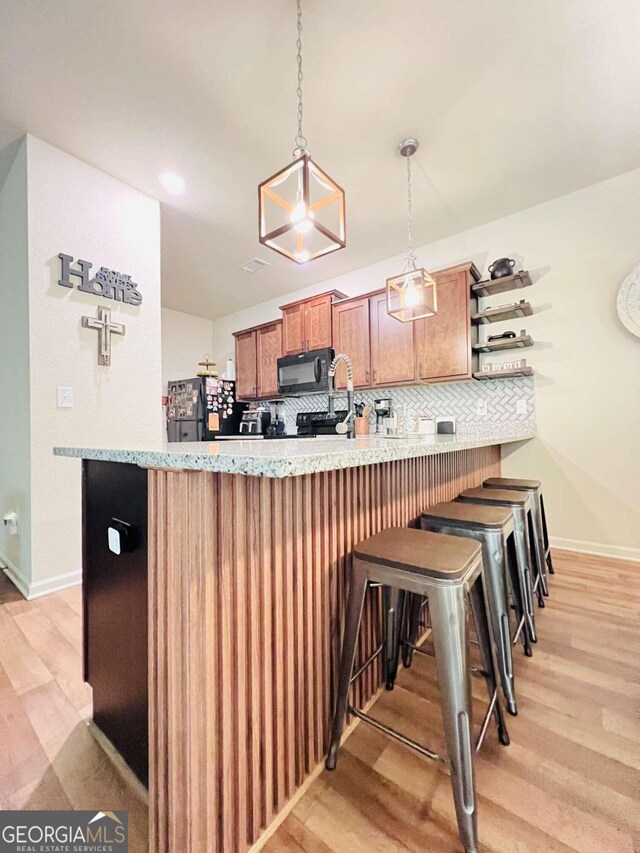 kitchen featuring backsplash, kitchen peninsula, pendant lighting, light wood-type flooring, and black appliances