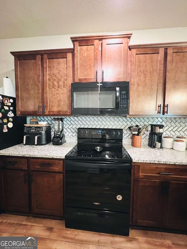 kitchen with black appliances, light stone countertops, light hardwood / wood-style flooring, and tasteful backsplash