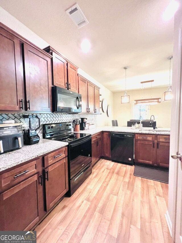 kitchen featuring light wood-type flooring, light stone counters, tasteful backsplash, hanging light fixtures, and black appliances