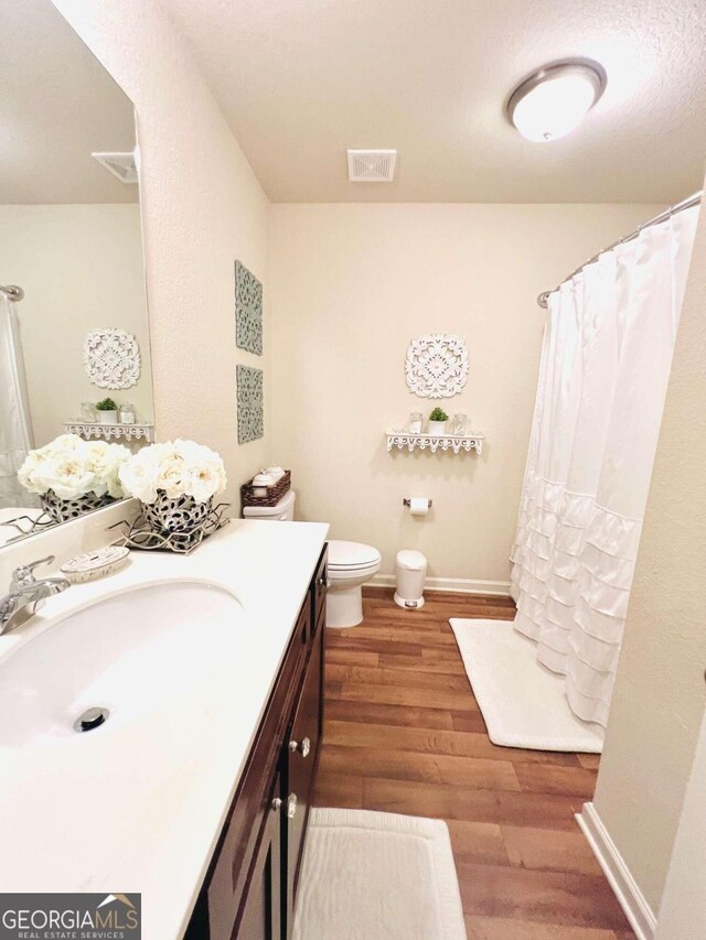 bathroom featuring hardwood / wood-style floors, walk in shower, vanity, and toilet