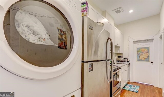 1313 Whitaker St, Savannah, GA 31401 - kitchen featuring washer / dryer, stainless steel appliances, white cabinets, light wood-style floors, and a sink