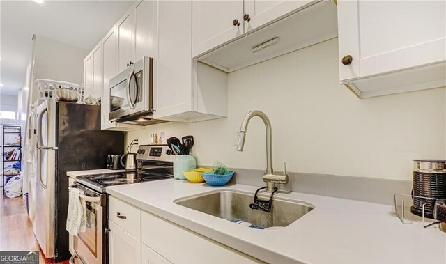 1313 Whitaker St, Savannah, GA 31401 - kitchen with appliances with stainless steel finishes, a sink, light countertops, white cabinetry, and wood finished floors