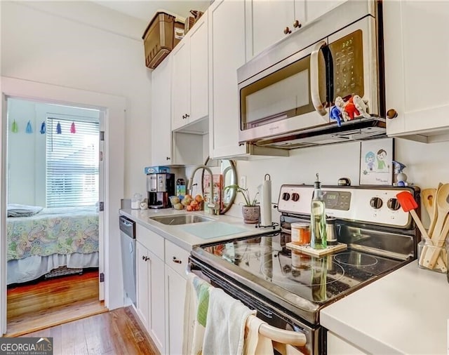 kitchen with stainless steel appliances, white cabinets, light wood-type flooring, and sink