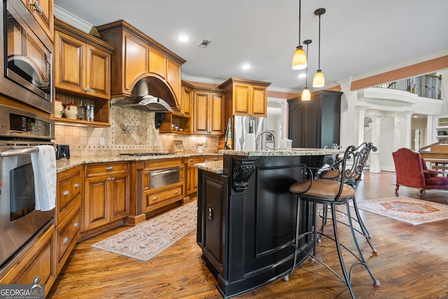 kitchen with dark wood-type flooring, stainless steel appliances, a center island with sink, and ornate columns