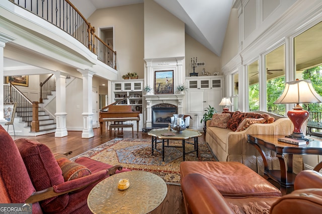 living room with ornate columns, hardwood / wood-style flooring, and high vaulted ceiling