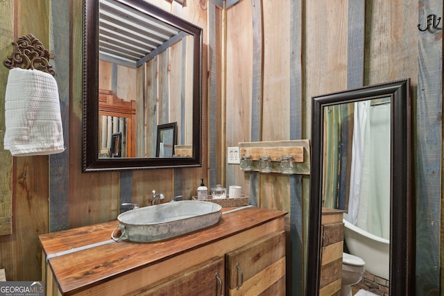 bathroom featuring vanity, wood walls, and toilet