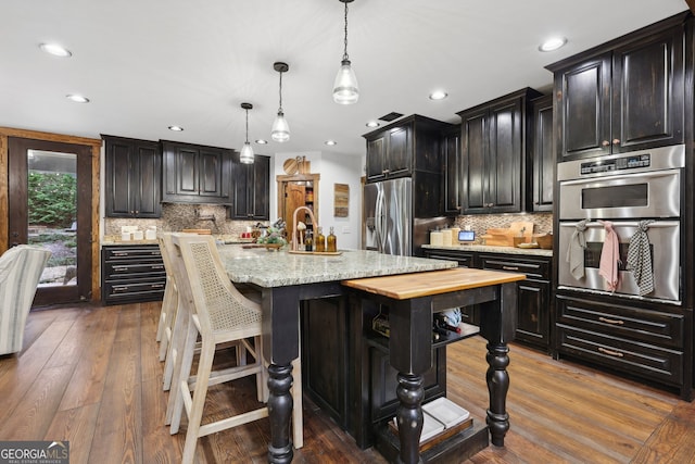 kitchen featuring pendant lighting, a kitchen bar, an island with sink, appliances with stainless steel finishes, and dark hardwood / wood-style flooring