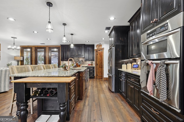 kitchen with stainless steel appliances, a kitchen island with sink, dark hardwood / wood-style floors, and decorative light fixtures