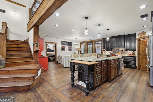 kitchen featuring pendant lighting, a center island with sink, dark hardwood / wood-style floors, decorative backsplash, and light stone counters