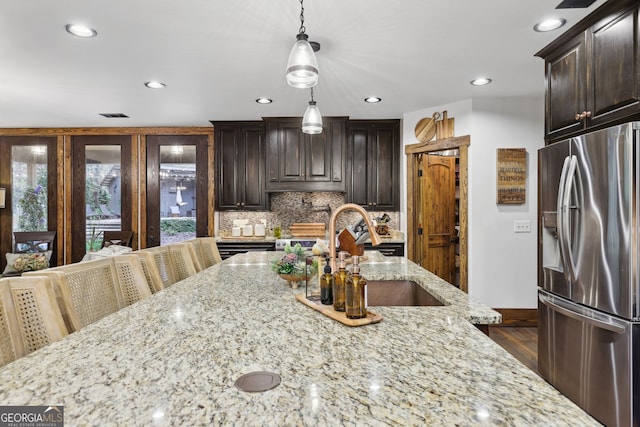 kitchen featuring backsplash, light stone counters, pendant lighting, and stainless steel refrigerator with ice dispenser