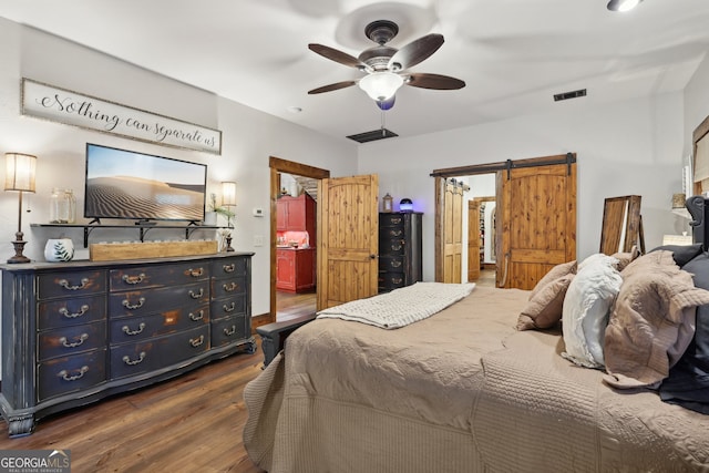 bedroom featuring ceiling fan, a barn door, and dark wood-type flooring