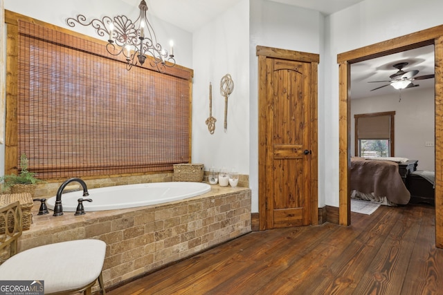 bathroom with hardwood / wood-style floors, ceiling fan with notable chandelier, and a relaxing tiled tub