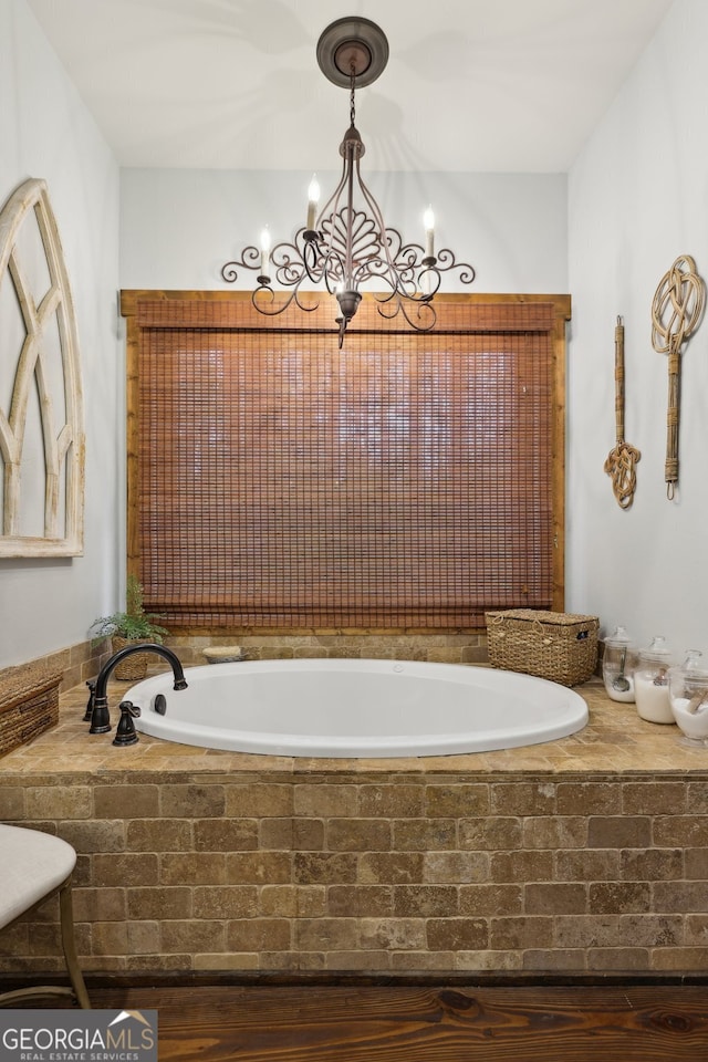 bathroom with wood-type flooring, a notable chandelier, and tiled tub