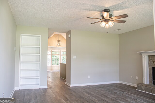 unfurnished living room featuring ceiling fan with notable chandelier, a stone fireplace, a textured ceiling, built in features, and dark hardwood / wood-style floors