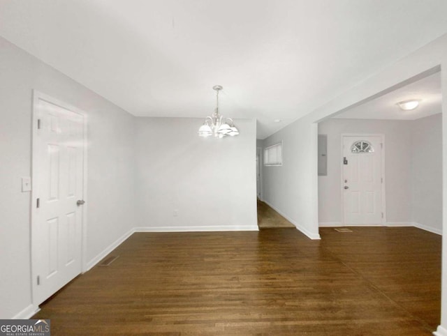 empty room with dark hardwood / wood-style flooring, a chandelier, and electric panel