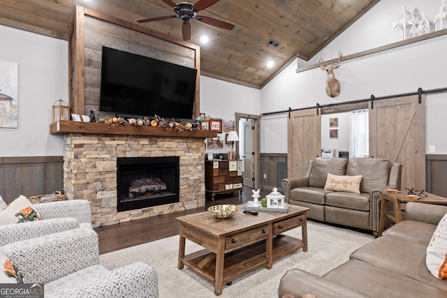 living room featuring wood ceiling, a barn door, a fireplace, wood walls, and ceiling fan