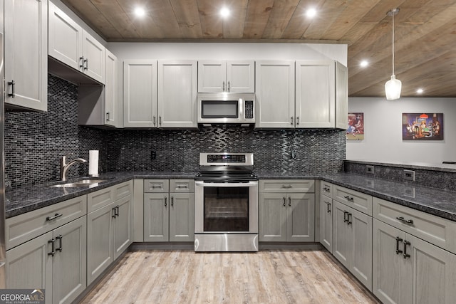 kitchen featuring hanging light fixtures, sink, dark stone counters, stainless steel appliances, and light wood-type flooring