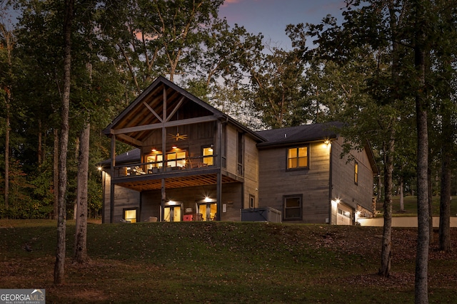 back house at dusk with a balcony and a yard