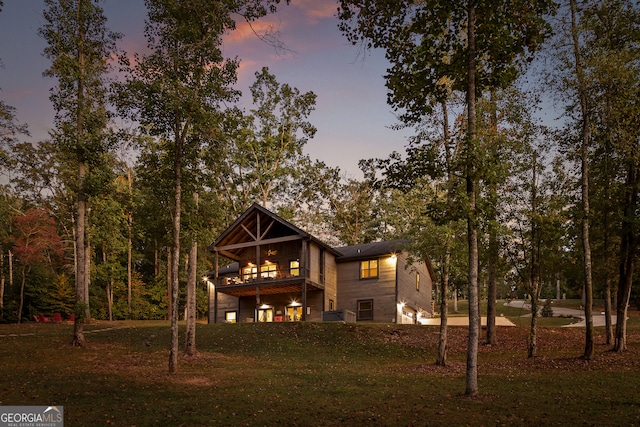 back house at dusk with a lawn and a balcony