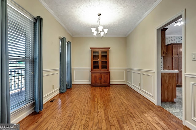 unfurnished room with a textured ceiling, a chandelier, light hardwood / wood-style floors, and crown molding