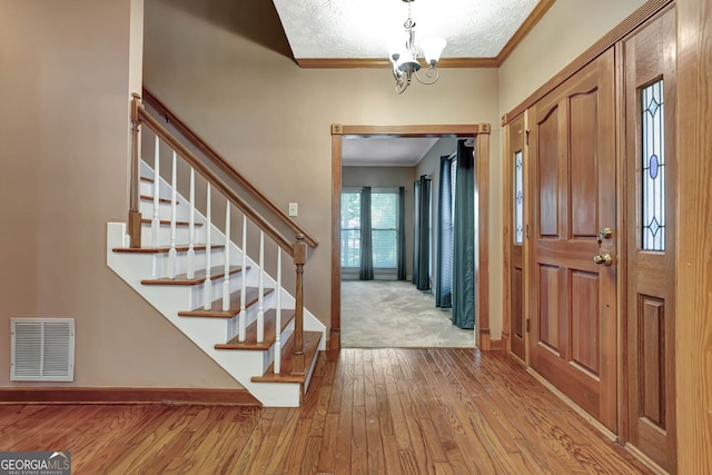 foyer entrance with light wood-type flooring, crown molding, a textured ceiling, and an inviting chandelier