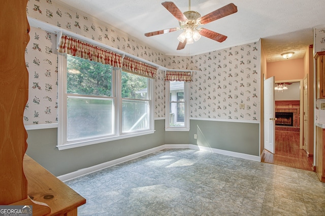 unfurnished room featuring a textured ceiling, ceiling fan, and a brick fireplace