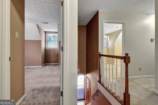 hallway featuring a textured ceiling and light carpet