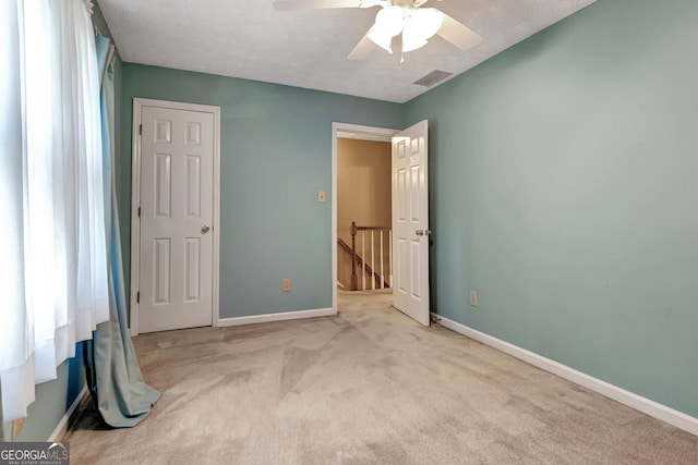 unfurnished bedroom featuring a textured ceiling, ceiling fan, and light colored carpet