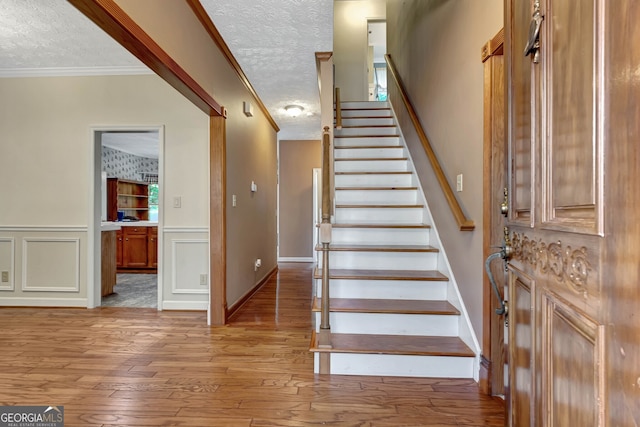 stairway featuring wood-type flooring, a textured ceiling, and crown molding