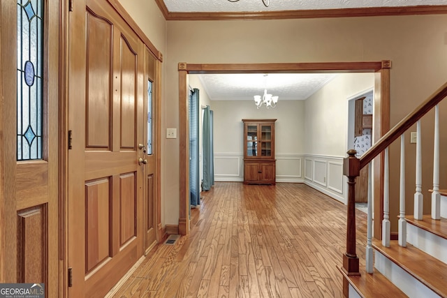 foyer entrance with a textured ceiling, light wood-type flooring, and crown molding