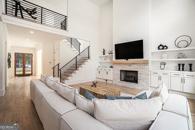 living room with wood-type flooring, a fireplace, a towering ceiling, and ornamental molding