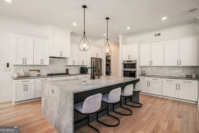 kitchen featuring light wood-type flooring, decorative backsplash, white cabinets, appliances with stainless steel finishes, and a center island with sink