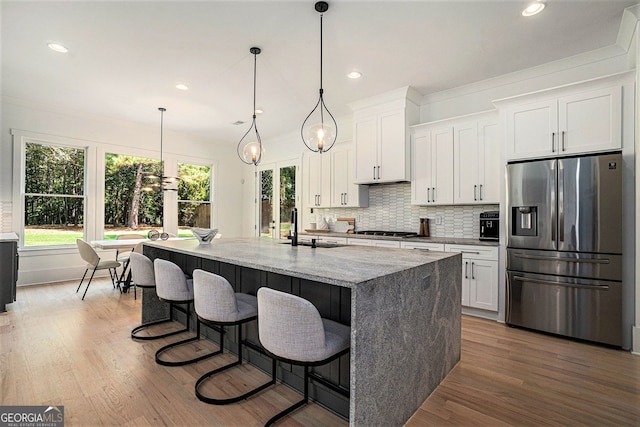 kitchen featuring a center island with sink, white cabinetry, appliances with stainless steel finishes, light stone countertops, and hardwood / wood-style floors