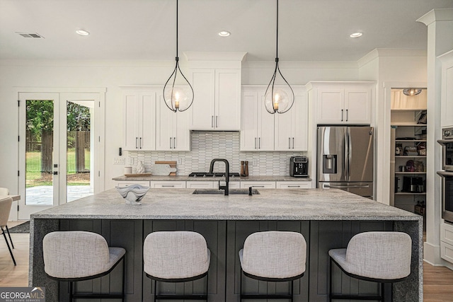 kitchen featuring hanging light fixtures, an island with sink, appliances with stainless steel finishes, and white cabinetry