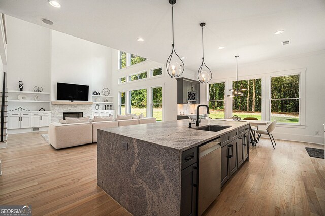 kitchen with an island with sink, light stone counters, sink, pendant lighting, and dishwasher