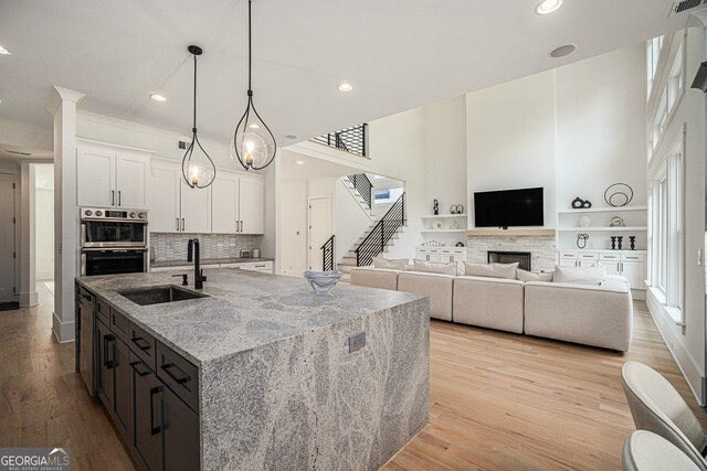 kitchen with light hardwood / wood-style flooring, white cabinets, a center island with sink, and light stone counters