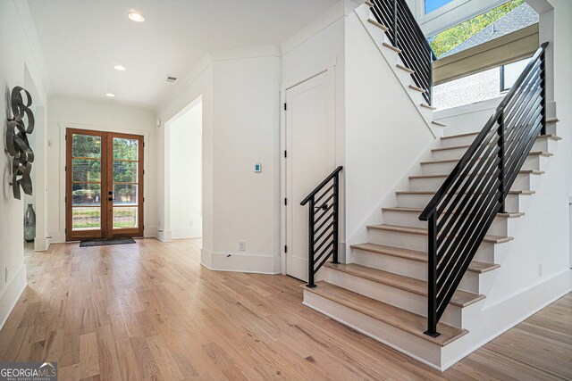 foyer entrance featuring french doors, crown molding, and light wood-type flooring