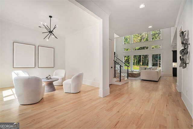 living area with ornamental molding, a high ceiling, an inviting chandelier, and light wood-type flooring